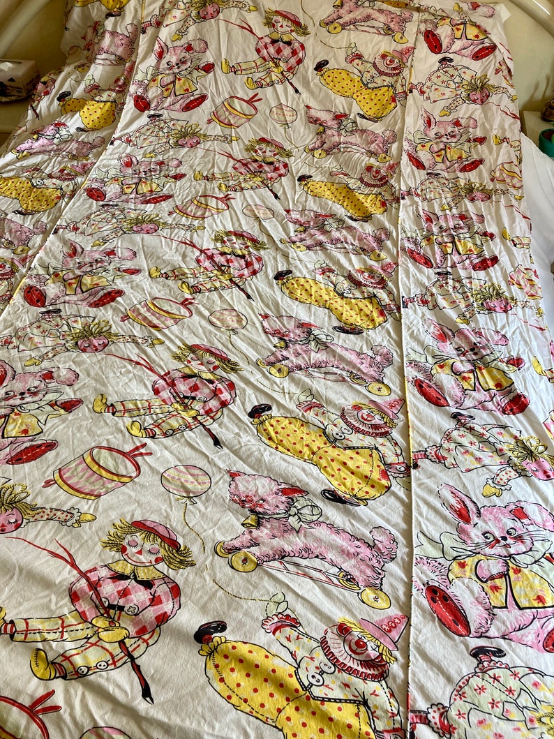 May include: A white cotton twin-sized bed sheet with a vintage pattern of clowns, teddy bears, and bunnies. The pattern is in shades of pink, yellow, red, and blue.
