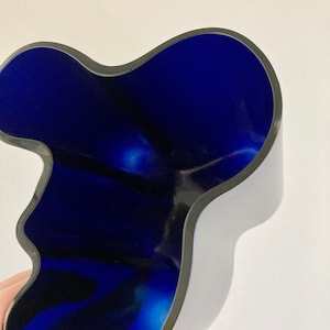 May include: A modern, abstract-shaped vase with a deep blue interior and a dark gray exterior. The vase has a smooth, glossy finish and a unique, organic form. The interior color contrasts with the exterior, creating a striking visual effect.