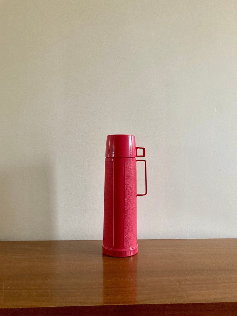 May include: A pink plastic thermos with a textured surface and a handle.