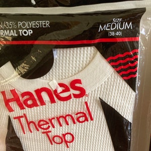 Peut inclure: Un haut thermique blanc Hanes dans un sac en plastique. Le sac porte le texte "35% Polyester Thermal Top" et "Taille M (38-40)".