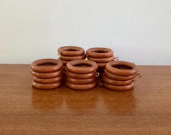Könnte beinhalten: Eine Sammlung von sechs hölzernen Gardinenringen in einem warmen, mittelbraunen Farbton. Jeder Ring ist kreisförmig mit glatter Oberfläche und einem kleinen Metallhaken. Die Ringe sind in kleinen Gruppen gestapelt.