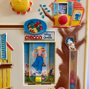 Puede incluir: Juguete vintage Chicco Play Center con un sol amarillo, un emblema de gallo y un ni&ntilde;o en un columpio. El juguete presenta una casa con un rat&oacute;n, un &aacute;rbol con un conejo y botones coloridos. El juguete es de pl&aacute;stico.