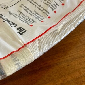 Peut inclure: Un paquet blanc avec du texte rouge qui indique "The Comforta" et "Hanes 65% coton/35% polyester blend." Le paquet contient un produit en coton blanc.