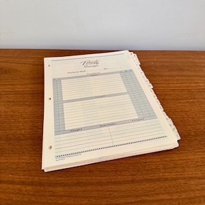 Könnte beinhalten: Ein cremefarbener "Priority Manager"-Planer mit Spiralbindung und Registerteilern. Die Planerseiten haben ein Rasterlayout mit Abschnitten für monatliche Prioritäten, persönliche Ziele und monatliche Auswertungen. Der Planer liegt auf einer Holzoberfläche.