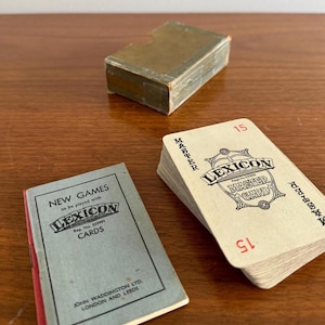 May include: A vintage Lexicon card game set, including a deck of cards, a rule book, and a box. The cards are marked with the word "Lexicon" and the number "15". The rule book is titled "New Games to be played with Lexicon Cards".