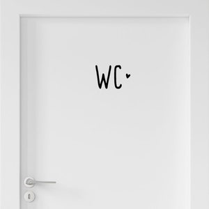 Peut inclure: Une porte blanche avec une poign&eacute;e en m&eacute;tal argent&eacute; et un autocollant noir au centre. L'autocollant affiche les lettres WC dans une police manuscrite simple, accompagn&eacute;es d'un petit c&oelig;ur noir plein positionn&eacute; &agrave; droite du texte.