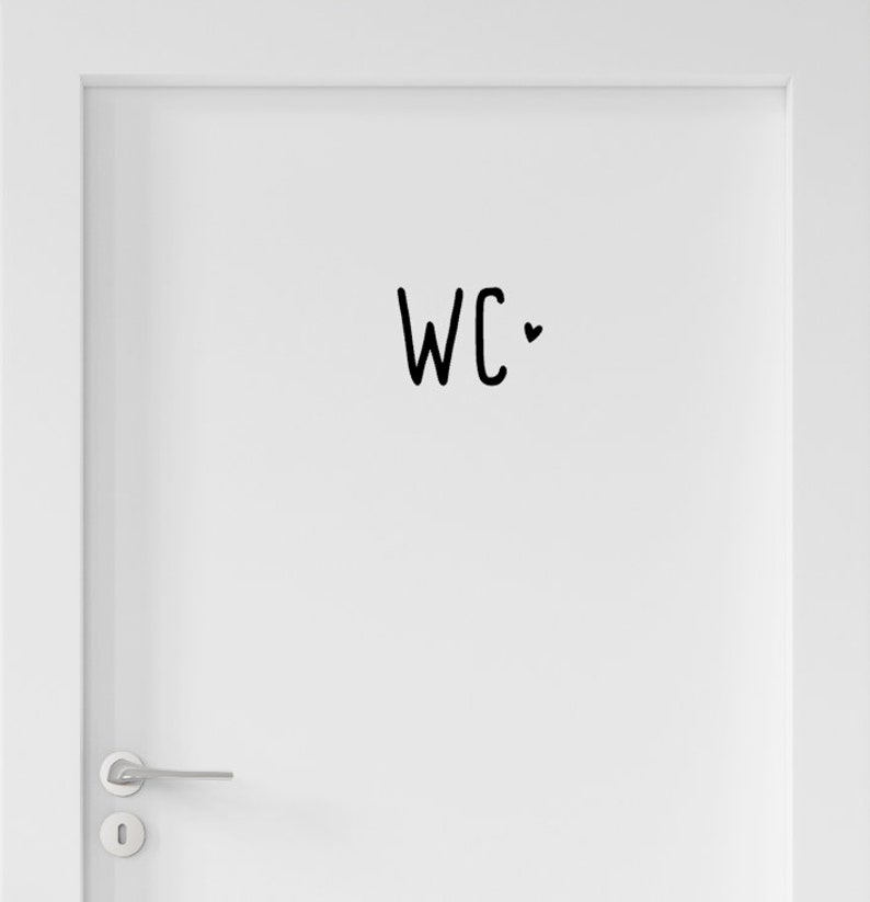Peut inclure: Une porte blanche avec une poign&eacute;e en m&eacute;tal argent&eacute; et un autocollant noir au centre. L'autocollant affiche les lettres WC dans une police manuscrite simple, accompagn&eacute;es d'un petit c&oelig;ur noir plein positionn&eacute; &agrave; droite du texte.