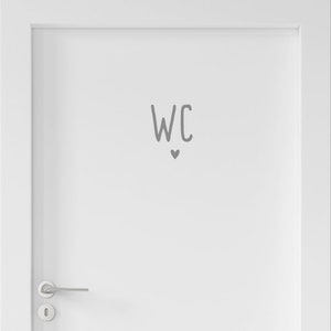 Peut inclure: Une porte blanche dot&eacute;e d'une poign&eacute;e en m&eacute;tal argent&eacute; et d'un autocollant gris au centre. L'autocollant affiche les lettres WC dans une police simple et arrondie, plac&eacute;es juste au-dessus d'une petite ic&ocirc;ne de c&oelig;ur gris solide centr&eacute;e.