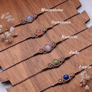 May include: Five bracelets featuring various gemstones, including moonstone, sunstone, kunzite, jade, and lapis lazuli. Each bracelet is crafted with brown cord and gold beads.