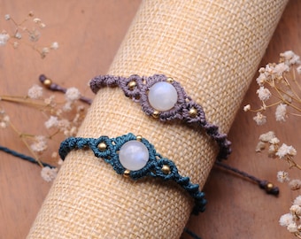 Puede incluir: Dos pulseras de macramé con cuentas de piedra lunar. Las pulseras están hechas con cordón azul oscuro y gris y cuentas doradas. Las cuentas de piedra lunar son blancas e iridiscentes.