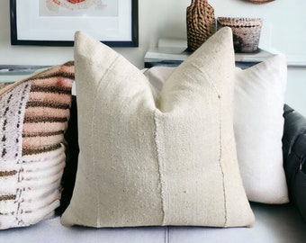 May include: A white throw pillow with a textured weave and a subtle seam down the center. The pillow is on a light gray couch with other pillows in the background.