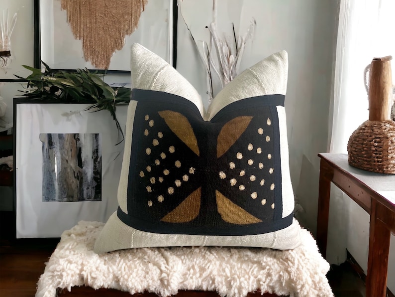 May include: A white linen pillow with a black and gold geometric pattern. The pattern features a stylized butterfly design with gold dots on a black background.