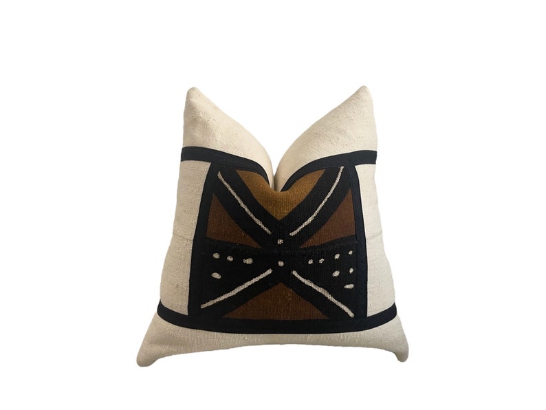 May include: A white pillow with a brown and black geometric pattern. The pattern features a large, stylized X shape with smaller circles and lines.