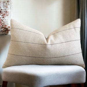 May include: A beige throw pillow with brown stripes. The pillow is sitting on a white bench.