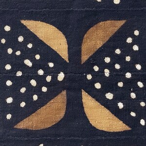 May include: A black fabric with a brown and white geometric pattern. The pattern is made up of four curved shapes that intersect in the center. The shapes are outlined in white and filled with brown. The background is black and has white dots scattered throughout.