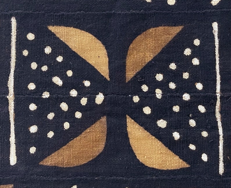 May include: A black fabric with a brown and white geometric pattern. The pattern is made up of four curved shapes that intersect in the center. The shapes are outlined in white and filled with brown. The background is black and has white dots scattered throughout.