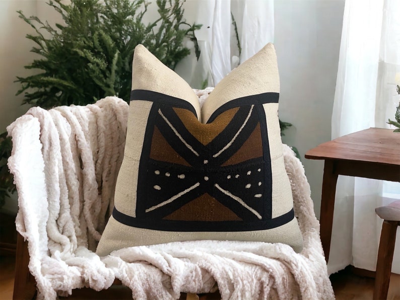 May include: A white throw pillow with a brown and black geometric pattern. The pillow is sitting on a white fluffy blanket.