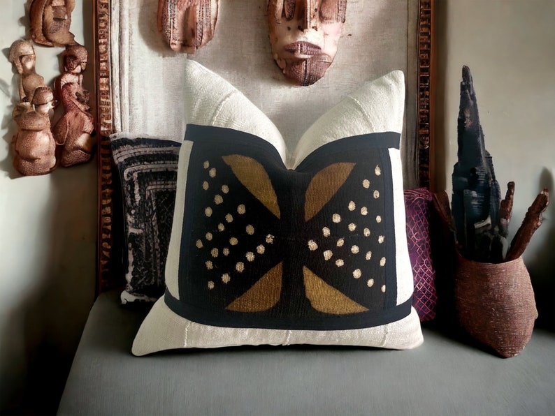 May include: A white throw pillow with a black and gold geometric pattern. The pattern features a large, stylized X shape with gold accents and black dots.