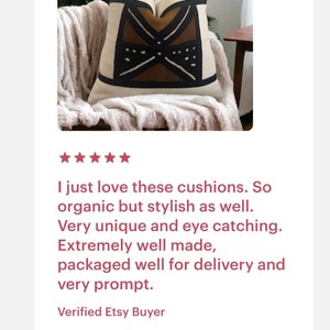 May include: A decorative throw pillow with a geometric pattern in shades of brown, black, and white. The pillow is made of a soft, natural fabric and is sitting on a fluffy white throw blanket.