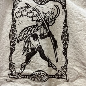 May include: Black and white illustration of a fairy-like creature with wings, holding a staff with flowers. The illustration is framed with a decorative border.