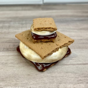 May include: A miniature s'more made of graham crackers, a white marshmallow, and chocolate.