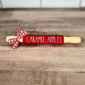 May include: Red rolling pin with a white "CARAMEL APPLES" inscription and a red and white gingham bow.