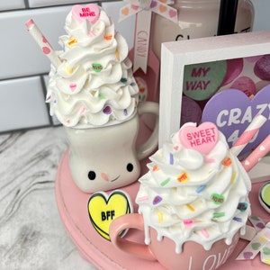 May include: A pink tiered tray decorated with Valentine's Day themed items. The tray features two mugs filled with whipped cream and candy hearts, a sign that says "My Way", and a sign that says "Crazy 4 You".