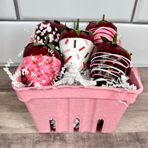 May include: A pink basket filled with chocolate-covered strawberries decorated with white and pink sprinkles. The strawberries are arranged in a single layer and are visible from the top.