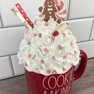May include: Red ceramic mug with white whipped cream, candy canes, and gingerbread men on top. The mug says "Cookie Baking Crew".