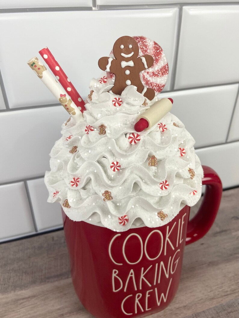 May include: Red ceramic mug with white whipped cream, candy canes, and gingerbread men on top. The mug says "Cookie Baking Crew".