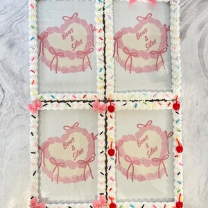 May include: Four white picture frames with a pink and white frosting design. Each frame has a pink heart with the text "Bows & Silos" inside. The frames are decorated with colorful sprinkles and red cherries.