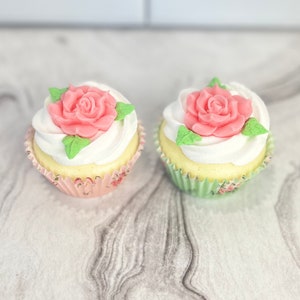 May include: Two cupcakes with white frosting and pink rose decorations. The cupcakes are in paper liners with floral patterns.