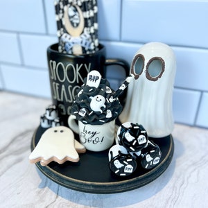May include: A black and white Halloween themed tiered tray with a ghost, a mug that says "Spooky Season", a mug that says "Hey Boo!" and a variety of black and white ghost-shaped decorations.