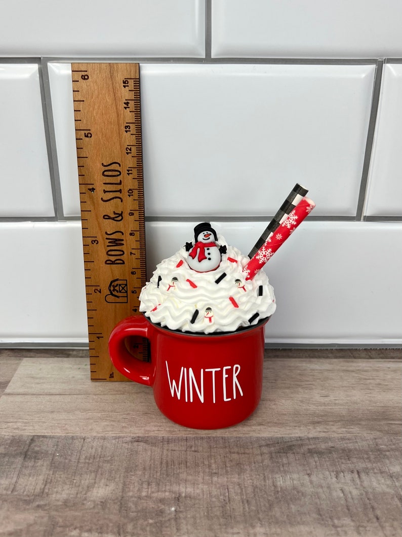Op de afbeelding: Rode keramische mok met witte slagroom en een sneeuwpop erop. De mok heeft de tekst "WINTER" aan de voorkant. Een gestreepte rietje zit in de mok.