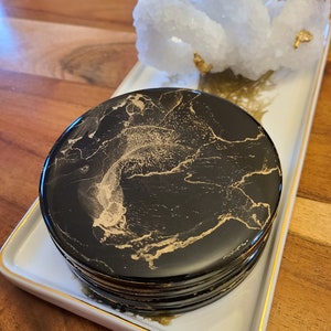 May include: A black and gold round trinket box with a marbled design. The box is on a white tray with a gold trim.