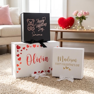 May include: Three Valentine's Day gift boxes. A black box with a teddy bear graphic and the text "Happy Valentine's Day Simone". A white box with the name "Olivia" and red hearts. A white box with the text "Madison Happy Valentine's Day".