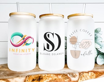 Pode incluir: Três copos de vidro fosco com tampas de bambu e canudos transparentes. Os copos apresentam diferentes designs: um símbolo de infinito com o texto "INFINITY CREATIVE STUDIO", um monograma "SD" com o texto "SLOANE DELANEY" e um desenho de linha de uma cafeteira com o texto "ELITE COFFEE ad elle".