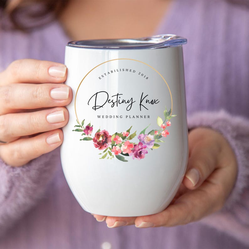 May include: White stainless steel wine tumbler with a gold circle and floral design. The text "Established 2018" and "Destiny Knox Wedding Planner" is printed on the tumbler.