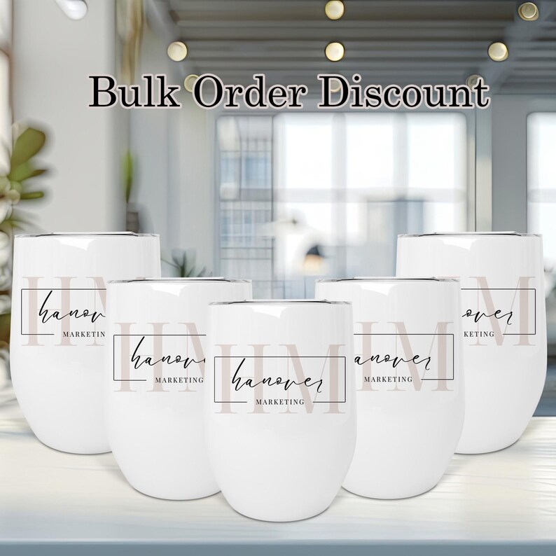 May include: Five white stainless steel tumblers with a black and white logo that says "Hanover Marketing" on each. The tumblers are arranged in a row on a table.