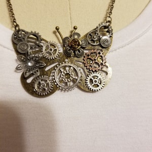 以下が含まれることがあります： チェーンが付いた銀と金の steampunk スタイルの蝶のネックレス。蝶は歯車やその他の金属部品でできています。