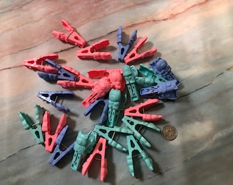 May include: A collection of colorful plastic clothespins in shades of pink, blue, and green. Some clothespins have animal-shaped designs. The clothespins are arranged on a marble-patterned surface.