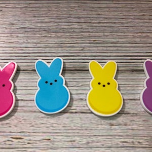 May include: Four colorful bunny-shaped marshmallow candies. The candies are pink, blue, yellow, and purple.
