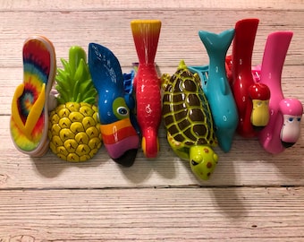 May include: A set of eight colorful plastic hair clips featuring a variety of tropical and ocean-themed designs, including a pineapple, toucan, fish, turtle, dolphin, and flamingo.