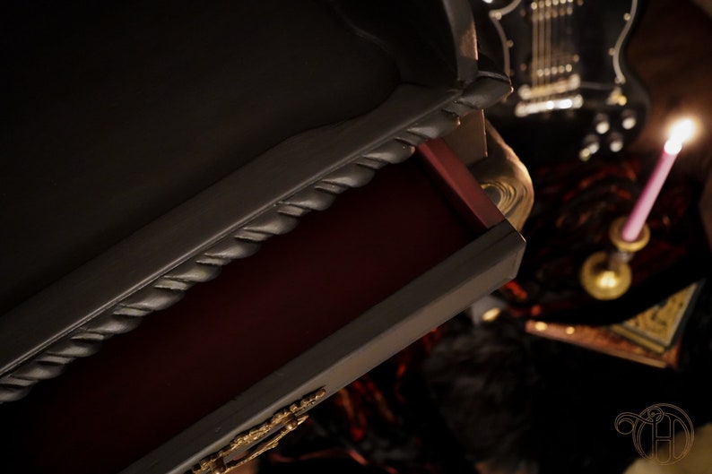 May include: A black dresser with a drawer open, revealing a red interior. The drawer has a rope-like design on the front edge. The dresser is in a dark room with a guitar and a candle in the background.
