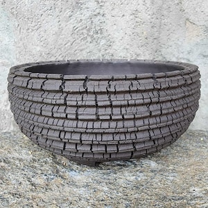 May include: A dark charcoal gray ceramic bowl featuring a deeply textured exterior with a cracked, grid-like pattern. The bowl has a wide, circular opening and a smooth, dark interior surface, showcasing a rugged, weathered appearance throughout.