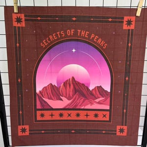 Pode incluir: Um tecido de parede castanho com o texto "SECRETS OF THE PEAKS" sobre uma cena de montanha. A cena apresenta um pôr do sol rosa e roxo sobre montanhas vermelhas. O design inclui estrelas e formas geométricas.