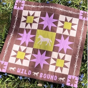May include: A square, brown quilt with a patchwork design featuring lavender stars, white triangles, and chartreuse squares. A white horse silhouette is centered on a chartreuse square. The words "WILD BOUND" are printed in lavender, along with horse silhouettes.