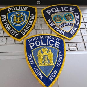 May include: Three embroidered police patches with yellow borders. One reads New York City Sanitation Police, another New York New Jersey Police N.Y.S.&W.R.Y., and the third Port Authority Police New York New Jersey, each featuring official state emblems.