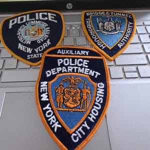 May include: Three embroidered uniform patches featuring the text Police Metro-North Commuter Railroad New York State, Bridge & Tunnel Triborough Authority, and Auxiliary Police Department New York City Housing with blue, orange, and white details.