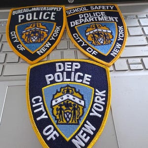 May include: Three embroidered patches featuring the City of New York seal. The top left patch reads Bureau of Water Supply Police, the top right reads School Safety Police Department, and the bottom patch reads DEP Police. All have yellow borders.